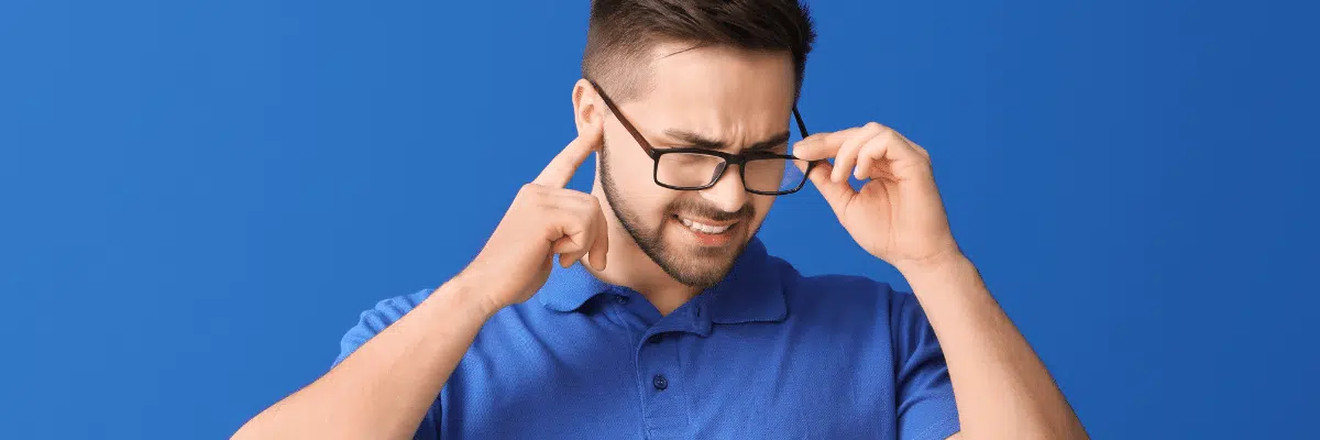 Man in blue shirt with glasses holding ears from noise